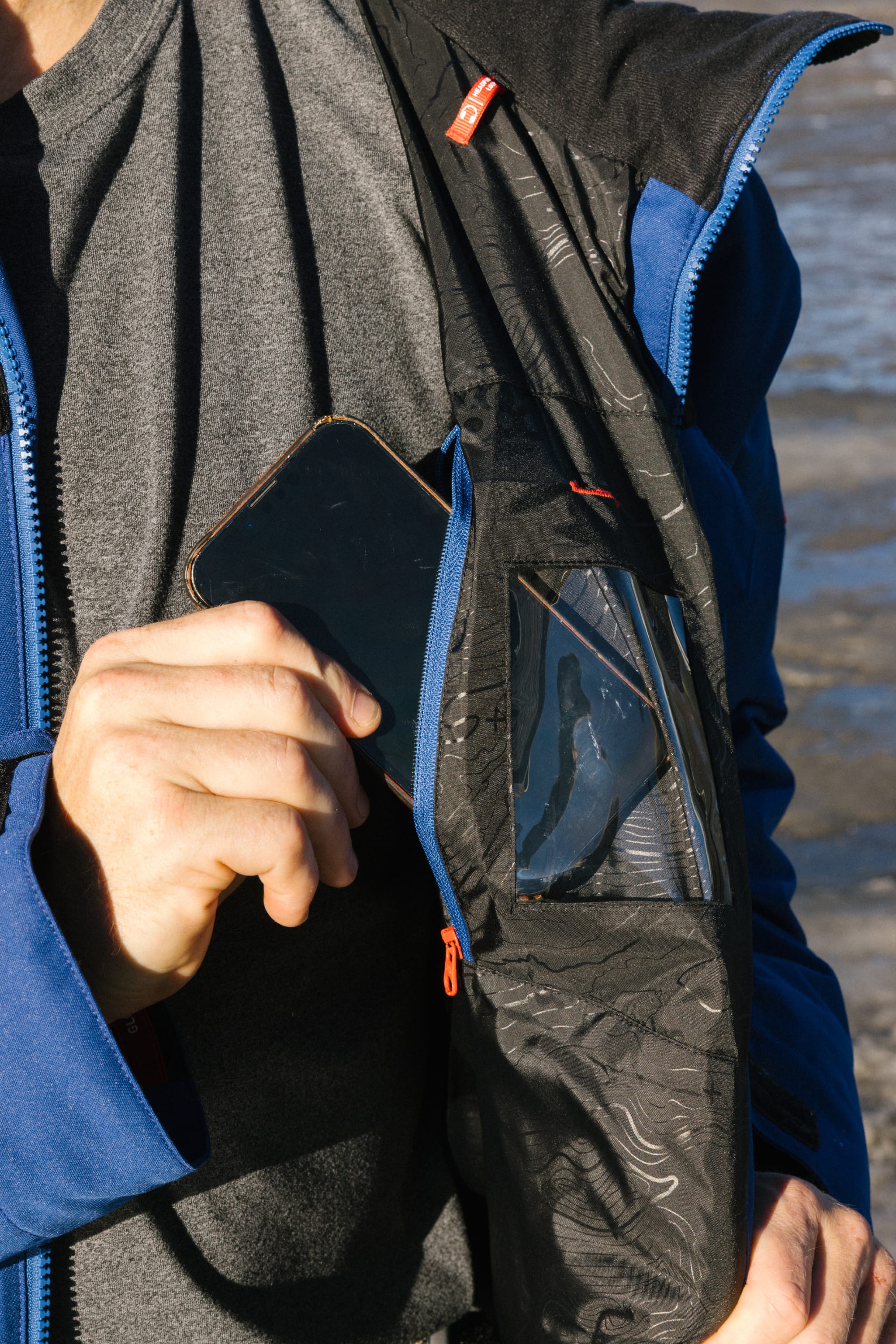 A man wearing the 686 Mens PBR Cooler Insulated Jacket pulls out a smartphone from the zippered inner chest pocket with a clear window inside the jacket.