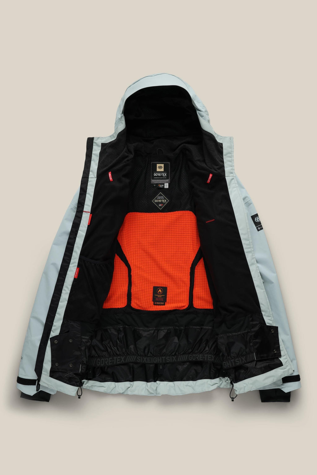 The 686 Men's GORE-TEX GT Thermagraph® Jacket by 686 is shown open, highlighting its black inner lining with an orange mesh back panel, multiple interior labels including a GORE-TEX tag, plus black cuffs and hem.