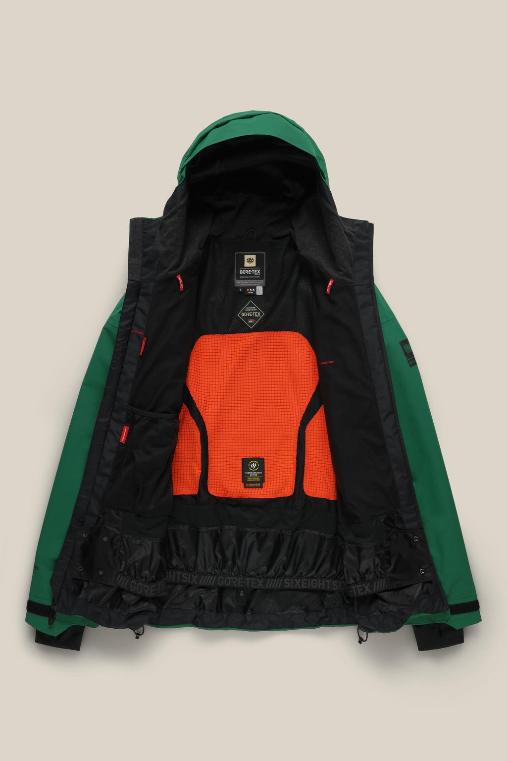 The 686 Men's GORE-TEX GT Thermagraph® Jacket is a green waterproof woven jacket with a hood, bright orange mesh back panel, black inner lining, neck and waist labels, and adjustable cuffs. Made by 686 with GORE-TEX material.
