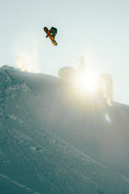 A snowboarder launches off a snowy slope, silhouetted against the bright sun as snow flies and he wears the 686 Men's GORE-TEX GT Thermagraph® Jacket from 686.