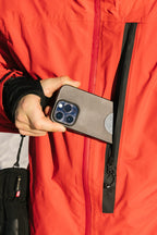 A man in a bright red 686 Men's GORE-TEX GT Thermagraph® Jacket unzips the vertical chest pocket and partially places a smartphone with a gray case inside.