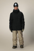 A person wearing the 686 Men's SMARTY® 3-In-1 Form Jacket, beige snow pants, gloves, boots, and a black helmet with goggles stands facing forward against a plain light background.