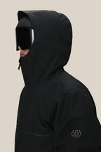 A person wearing a black 686 Men's SMARTY® 3-In-1 Form Jacket with the hood up, large black ski goggles, and visible 686 branding on the chest and sleeve.