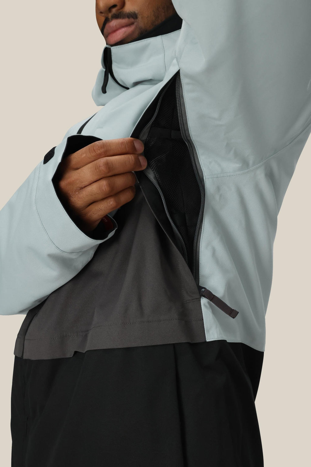 A person unzips the underarm vent of a light gray and black 686 Men's SMARTY® 3-In-1 Form Jacket, revealing its mesh lining.