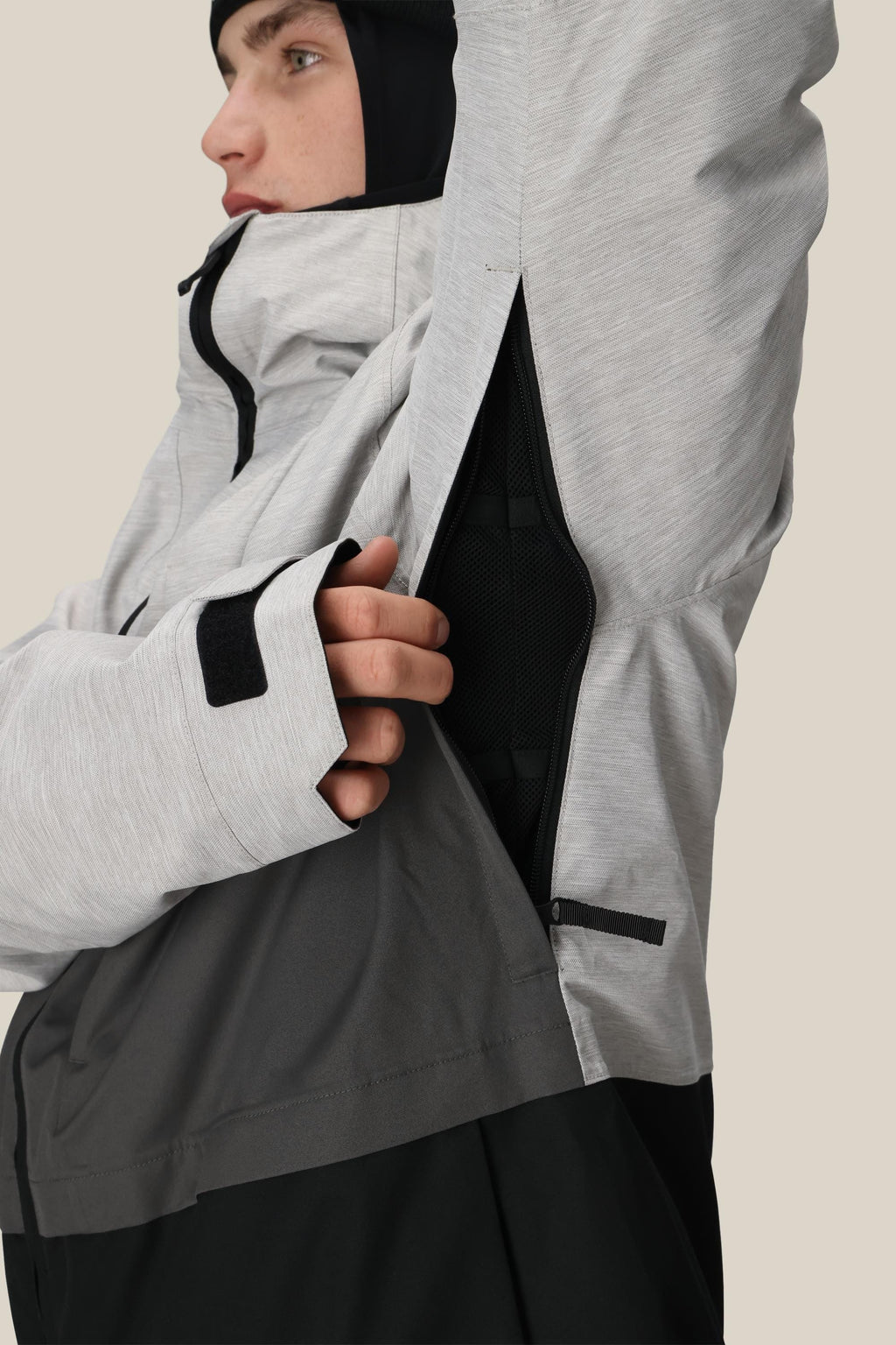 A person wearing the 686 Men's SMARTY® 3-In-1 Form Jacket in light gray with a black inner layer unzips a side vent, showing the black lining. The 686 polyester waterproof jacket has sleeve thumb holes, and the person wears a black hood or balaclava.