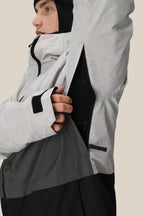 A person wearing the 686 Men's SMARTY® 3-In-1 Form Jacket in light gray with a black inner layer unzips a side vent, showing the black lining. The 686 polyester waterproof jacket has sleeve thumb holes, and the person wears a black hood or balaclava.