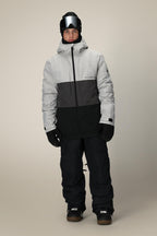A man stands facing forward against a plain beige background, wearing the 686 Men's SMARTY® 3-In-1 Form Jacket in black/gray, along with black snow pants, black gloves, ski goggles, and a black beanie.