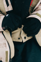 A person wearing black gloves fastens a snap button on the 686 Mens GORE-TEX Core Shell Jacket. Only their hands and part of the 686 jacket are visible.