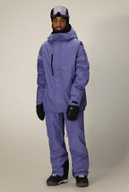 A person stands facing forward against a light background, wearing the 686 Mens GORE-TEX Core Shell Jacket in purple, matching pants, black gloves and boots, with ski goggles resting on their forehead.