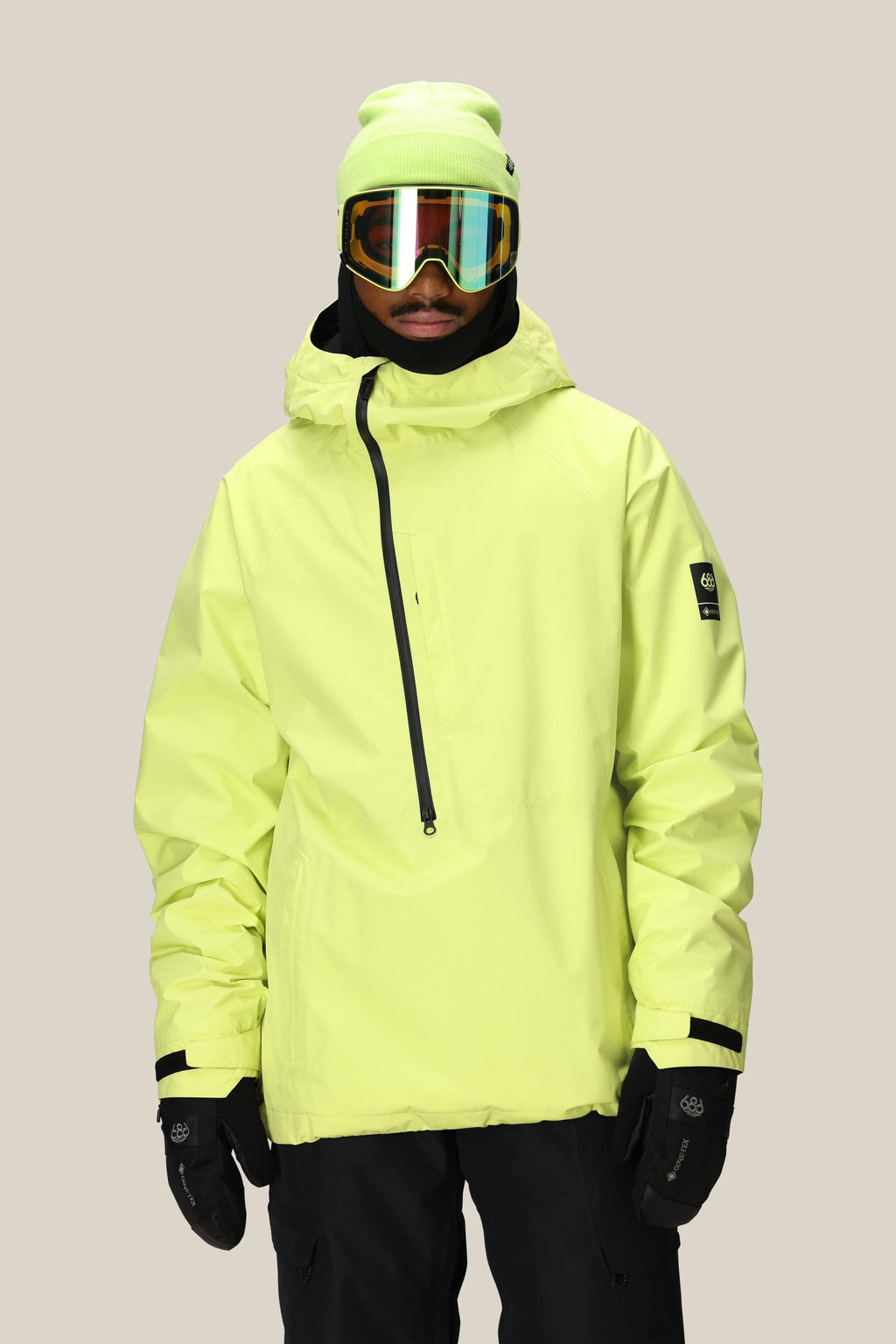 A person wearing the 686 Mens GORE-TEX Fragment Shell Anorak in neon yellow, black gloves, black snow pants, a neon yellow beanie, and reflective ski goggles stands facing forward against a plain light background.
