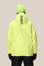 A person stands facing away against a plain beige background, wearing the 686 Mens GORE-TEX Fragment Shell Anorak in bright yellow with GORE-TEX on the hood and a matching yellow beanie.