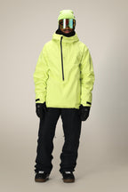 A person stands facing forward wearing the 686 Mens GORE-TEX Fragment Shell Anorak in light yellow, black snow pants, black gloves and boots, a yellow-green beanie, and reflective ski goggles against a plain background.