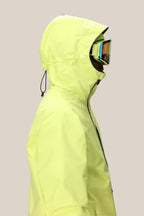 Person in profile wearing the 686 Mens GORE-TEX Fragment Shell Anorak in bright yellow with hood up and drawstring cinched, plus reflective ski goggles, against a plain beige background.