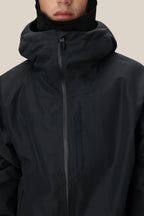 A man wears the 686 Mens Gateway Shell Jacket, a black waterproof style with a high collar and front zipper, shown from the shoulders up against a plain beige background.
