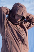 A person wearing the 686 Mens Gateway Shell Jacket adjusts their hood in a snowy, sunlit outdoor setting. Their face is partially visible as they look directly at the camera.