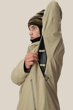 A man in a 686 Mens Gateway Shell Jacket and a striped beanie unzips the mesh-lined underarm vent, showcasing the jackets ventilation feature against a plain, light background.