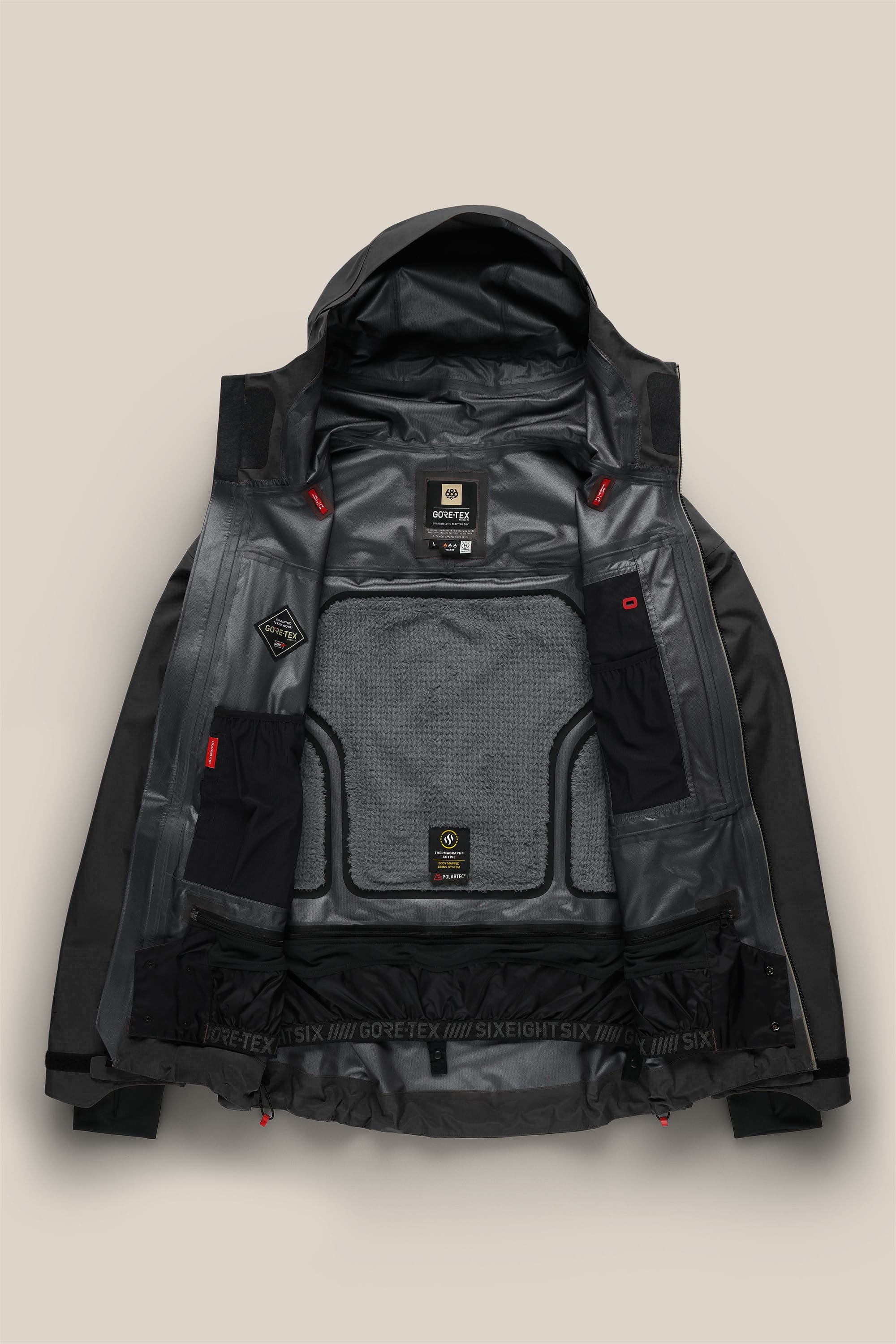 The 686 Men's GORE-TEX 3L ATV Thermagraph® Jacket—shown in black and laid flat on a beige background—displays its interior lining, mesh pockets, labels, and technical features.