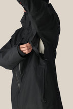 A man in a 686 Men's GORE-TEX 3L ATV Thermagraph® Jacket unzips an underarm vent, showing part of a light inner layer. The black polyester jacket by 686 features multiple zippers and a high collar.