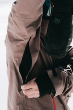 A person wearing the 686 Men's GORE-TEX 3L ATV Thermagraph® Jacket and black gloves is unzipping a sleeve pocket, with their hand and the zipper in focus while the background remains blurred.
