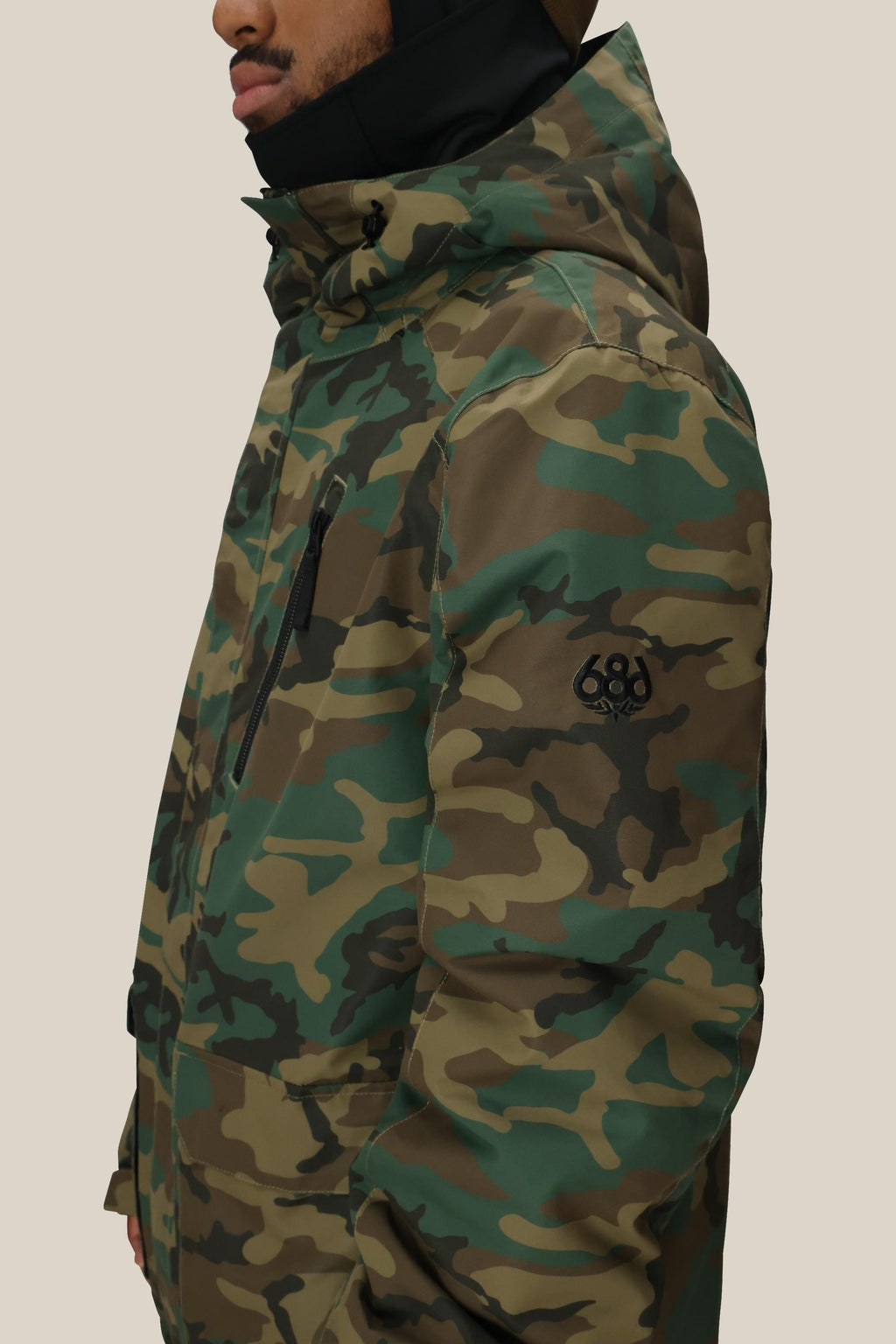 A person wearing the 686 Men's Nightline™ Insulated Jacket in green and brown, featuring a black 686 logo on the sleeve, stands sideways against a plain background.