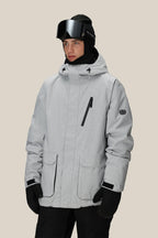 A person wearing the 686 Men's Nightline™ Insulated Jacket in light gray, paired with black gloves, black ski goggles, and a black hat, stands against a plain beige background.