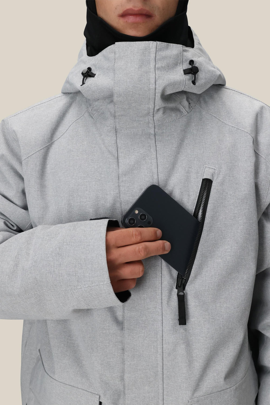 Wearing the 686 Men's Nightline™ Insulated Jacket with the hood up, a person slips a black smartphone into the chest pocket, their lower face visible.
