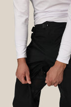 A person wearing a white long-sleeve shirt and 686 Mens GORE-TEX Core Shell Pant is unzipping a mesh-lined thigh vent. The photo is cropped above the shoulders.
