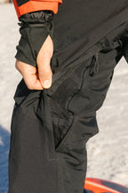 A person unzipping a mesh vent on the side of 686 Men's GORE-TEX Dispatch™ Shell Pant, standing on snow.