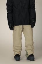 A person wearing a black jacket, black gloves, 686 Men's Quantum Thermagraph® Pant in beige by 686, and dark snow boots stands against a neutral background. The upper part of the face and head are not visible.