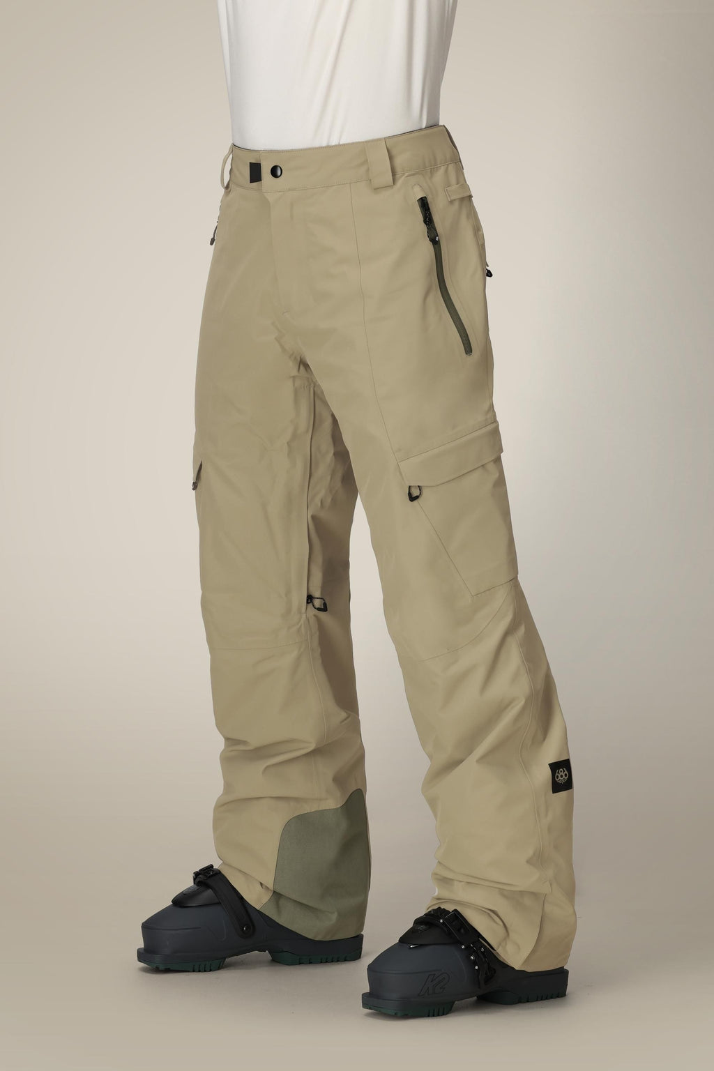 A person wearing 686 Men's Quantum Thermagraph® Pant in beige with black zippers and black snowboard boots, shown from waist down against a plain light background.