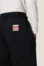 A person wears the 686 Dojo® GORE-TEX Pant by 686, featuring a colorful abstract patch on the back pocket, with a white long-sleeve shirt tucked in and their hand in the pocket.