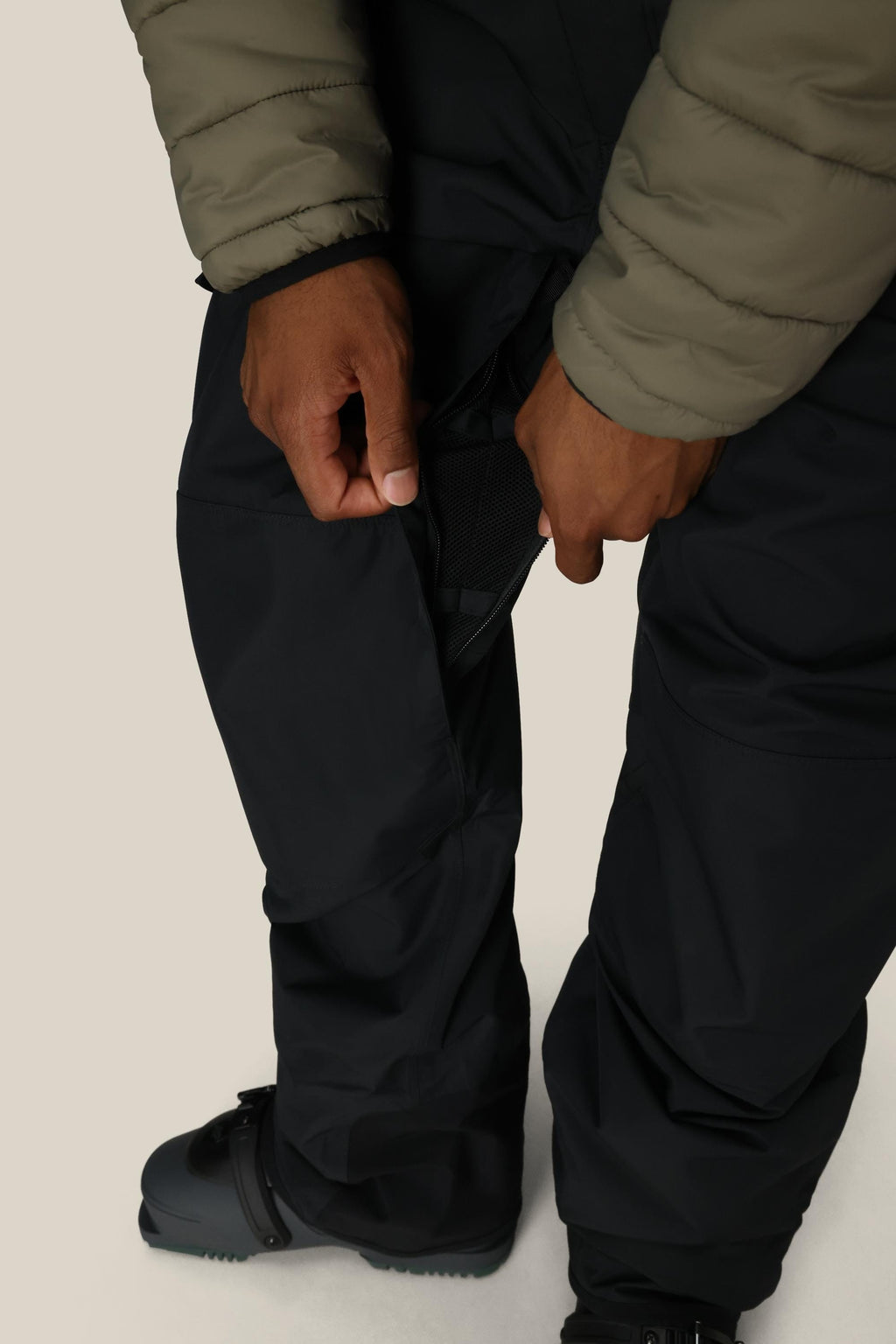 A person wearing 686 Men's 20K Hot Lap™ Shell Bib is unzipping a side vent to reveal black mesh. Only their hands, lower body, and boots are visible.