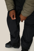 A person wearing 686 Men's 20K Hot Lap™ Shell Bib is unzipping a side vent to reveal black mesh. Only their hands, lower body, and boots are visible.