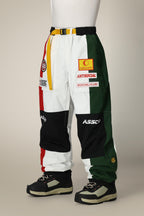 Wearing 686 Mens ASSC F1 Shell Pant by 686, featuring bold red, white, yellow, green, and black color-blocked panels with standout patches and logos, paired with black and beige sneakers. Upper body not shown.
