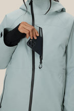 A woman wearing the 686 Women's Hydra™ Thermagraph® Jacket in light gray slips a black smartphone into the jacket's zippered chest pocket.