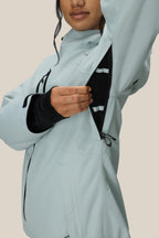 A woman in the 686 Women's Hydra™ Thermagraph® Jacket by 686 unzips an underarm vent to reveal black mesh lining. Her face is partly visible against a plain beige background.