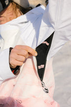 A person wearing the 686 Women's Hydra™ Thermagraph® Jacket in white and pink unzips an underarm ventilation pocket, revealing black mesh inside, with snow in the background.