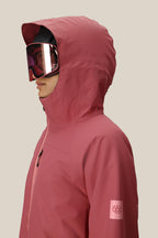 A person in a pink 686 Women's Hydra™ Thermagraph® Jacket and pink ski goggles faces left against a beige background. The waterproof jacket, by 686, displays the brand's logo on the sleeve.