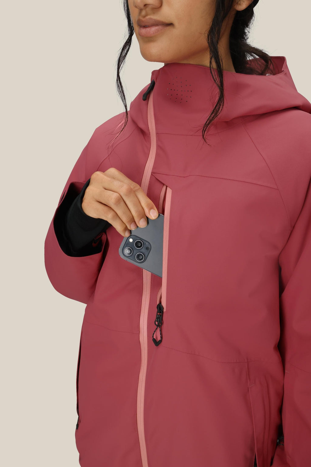 A woman in a 686 Women's Hydra™ Thermagraph® Jacket, pink and waterproof, with partially visible face and dark hair tied back, places a smartphone into the chest pocket.