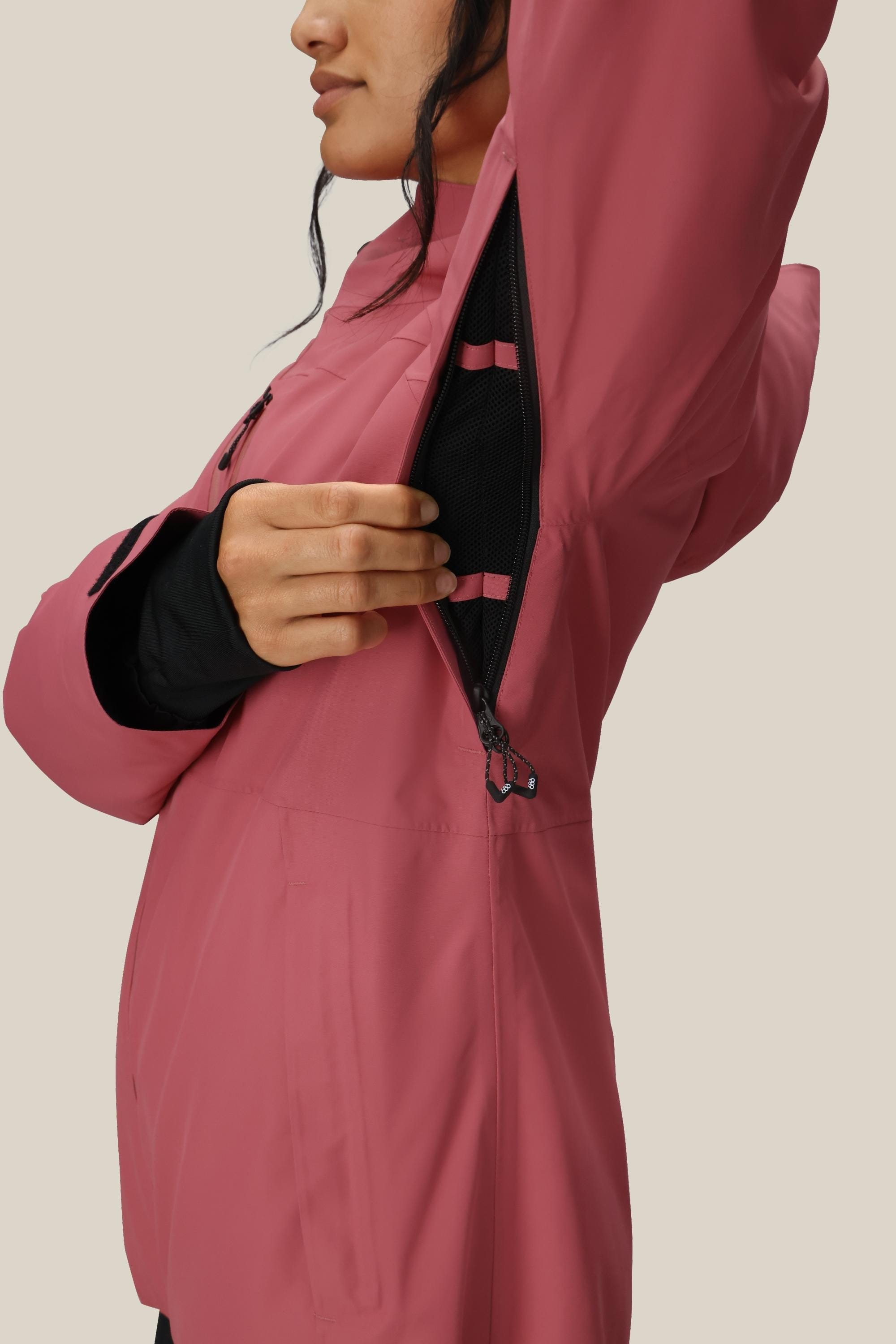 A person wearing the 686 Women's Hydra™ Thermagraph® Jacket unzips an underarm vent, revealing a black mesh lining. The background is plain and neutral.