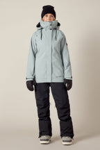 A person stands facing forward, wearing the 686 Women's SMARTY® 3-In-1 Spellbound Jacket by 686, black snow pants, black gloves, a black beanie, and gray winter boots against a plain light background.