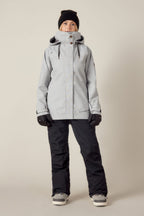 A person faces forward in a 686 Women's SMARTY® 3-In-1 Spellbound Jacket, black gloves, black pants, winter boots, and a black beanie against a plain light background.