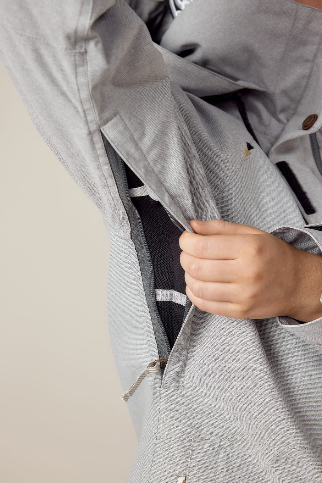 A hand pulls open a zippered vent under the arm of the 686 Women's SMARTY® 3-In-1 Spellbound Jacket in light gray, revealing mesh lining inside and highlighting jacket detail.
