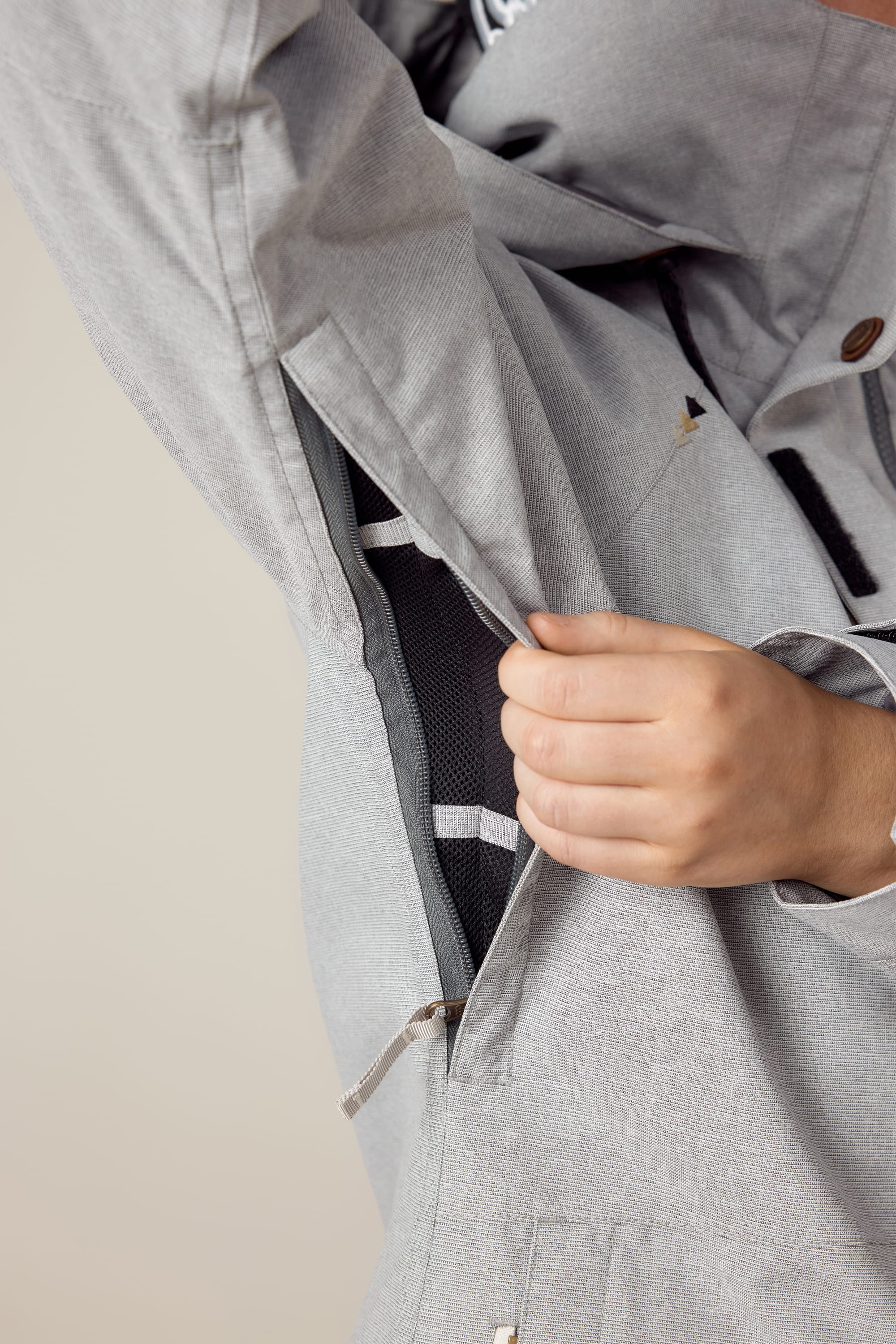 A hand pulls open a zippered vent under the arm of the 686 Women's SMARTY® 3-In-1 Spellbound Jacket in light gray, revealing mesh lining inside and highlighting jacket detail.