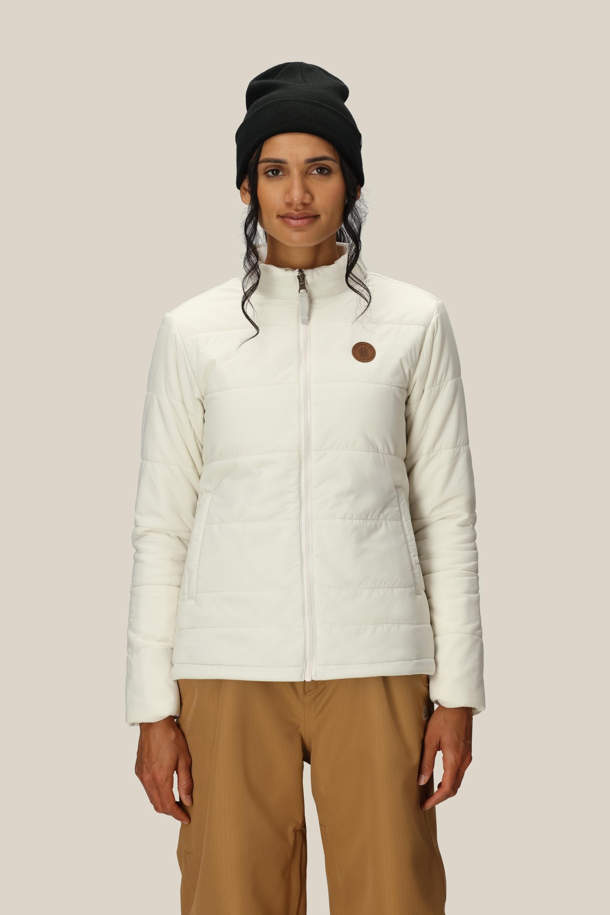A person wearing the 686 Women's SMARTY® 3-In-1 Spellbound Jacket in white stands against a plain beige background, facing forward with a neutral expression.
