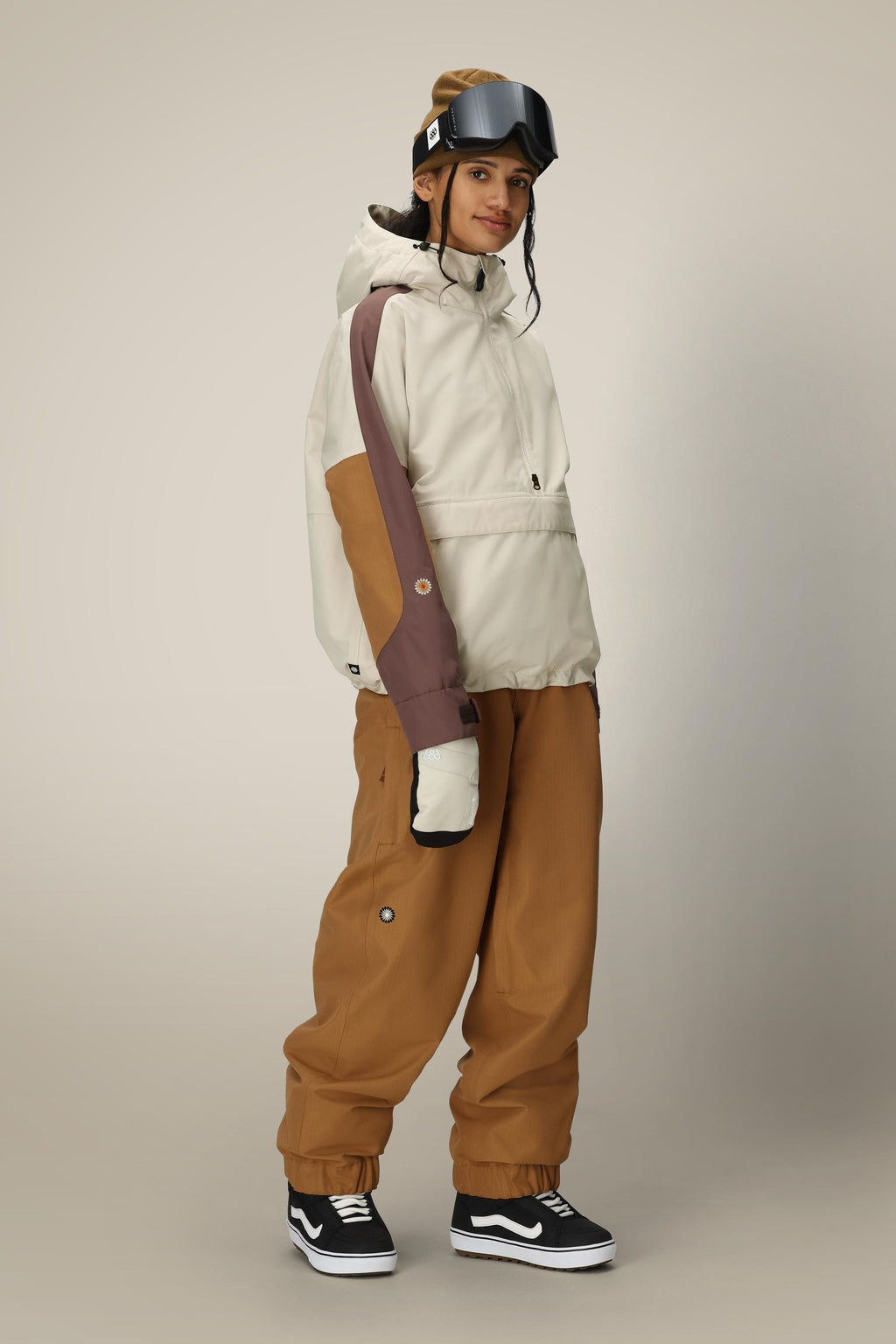 A person wearing the 686 Women's Outline™ Shell Anorak, matching pants, ski gloves, goggles on their head, and black Vans sneakers stands against a plain light background.