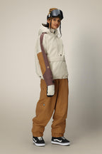 A person wearing the 686 Women's Outline™ Shell Anorak, matching pants, ski gloves, goggles on their head, and black Vans sneakers stands against a plain light background.