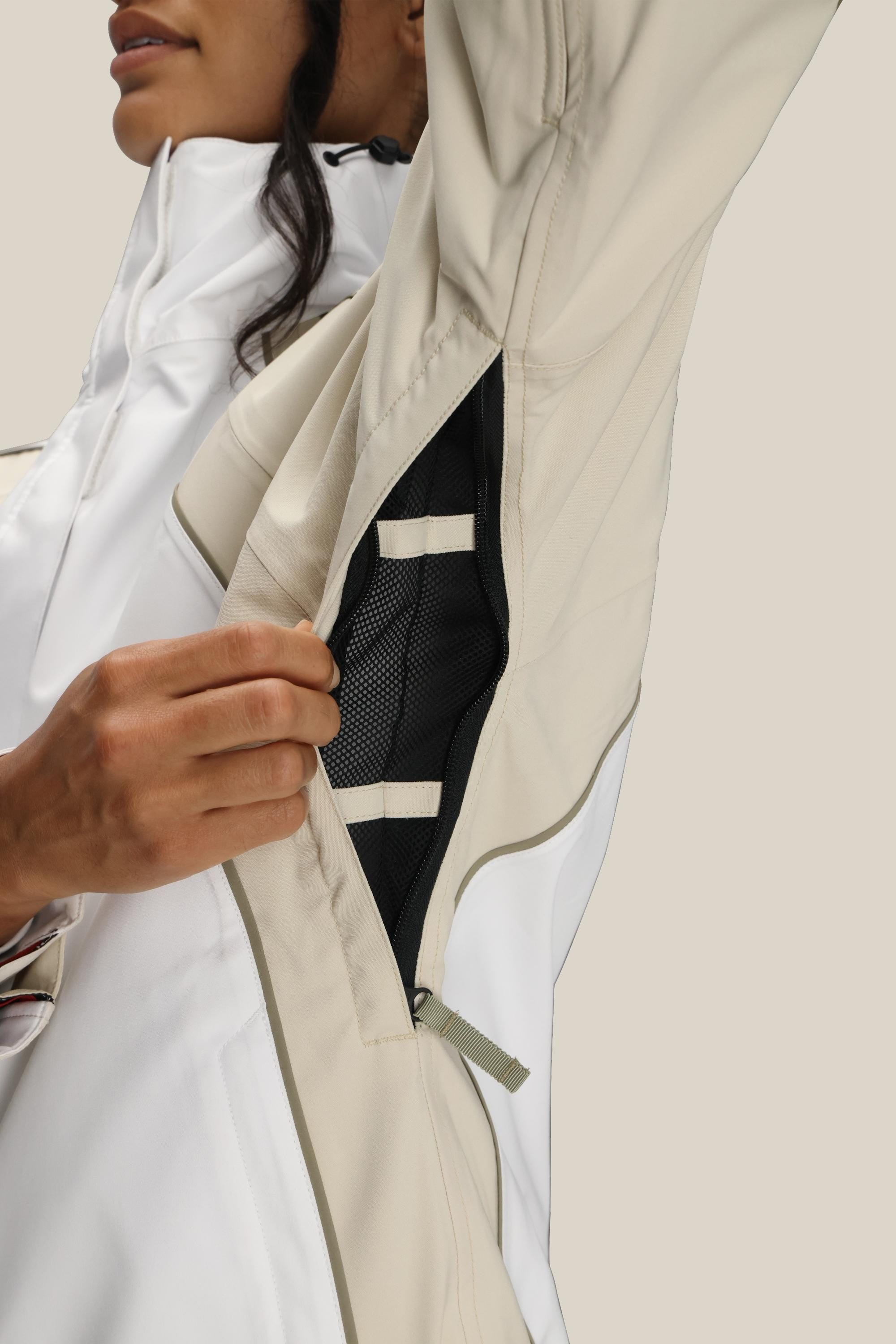 A woman wearing the 686 Women's Hologram™ Shell Jacket opens its mesh-lined underarm vent zipper, highlighting the breathable feature of this waterproof 686 jacket.