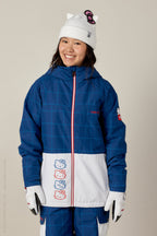 A smiling young woman wears the 686 Women's Athena™ Insulated Jacket by 686, paired with matching pants, white gloves, and a white beanie with cat ears and a bow.