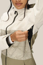A person in the 686 Women's Athena™ Insulated Jacket, featuring a two-tone geometric pattern, unzips an underarm vent to reveal the mesh lining. Only their lower face and upper body are visible.